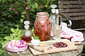 Homemade rose liqueur made from petals and fruits in a glass, balloon-shaped carafe and steeping in a flip-top jar