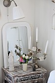 Madonnenfigur, verzierter Kerzenständer im Shabby-Stil und Frühlingsblumenstrauss vor Spiegelhintergrund auf Antiktischchen im Used-Look