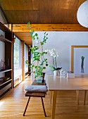Holzbank mit Kissen und Blumentopf vor Tisch in offenem Wohnraum mit Holzdecke