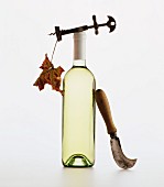 A bottle of white wine with a corkscrew, vine leaf and a knife