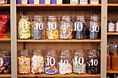 Assorted sweets in open storage jars, labelled with the price per item, on wooden shelving