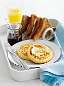 Crumpets mit Butter, Toast, Marmelade und Orangensaft zum Frühstück