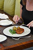 A woman eating a bacon wrapped meatloaf, herbed potatoes, green beans