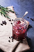 Jar of plum and juniper jam on dark background