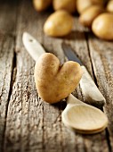 Heart-shaped potato, a wooden spoon and a knife on a wooden surface