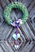 Willow wreath with purple flowers and decorative hearts on rustic front door