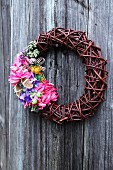 Wicker wreath with multicoloured flowers on wooden wall