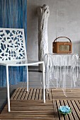White metal chair with punched floral pattern on back next to retro radio on plexiglass table in shape of draped tablecloth