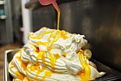 Freshly made vanilla ice cream being drizzled with mango and passion fruit sauce