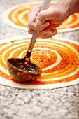 Pizza base being spread with tomato sauce