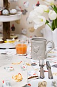 Napkin and tablecloth with colourful hen pattern and grey mug with hen-motif relief on table set for Easter