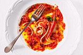 A plate with the remains of spaghetti with tomato and chilli sauce