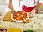 A chef cutting a pizza into portions using a pizza wheel