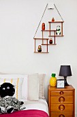 Jugendbett mit schwarzweisser Kuschelpuppe und Retro Holzkommode; an der Wand eine Art minimalistischer Setzkasten mit Figürchen