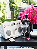 Stereo system and iPod next to liqueur glass and bottle of vodka in front of pink bouquet on black side table