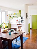 Open-plan, white kitchen with green door elements and dark wooden dining table