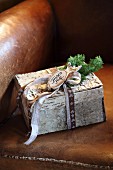 Small festive parcel decorated with birch bark and ribbon on leather armchair