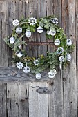 Christmas wreath of fir branches with crocheted stars and knitted baubles hanging on rustic wooden door