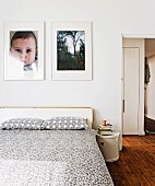 White and grey patterned bedspread and pillows on double bed below photos on wall; open door to one side with view into hall