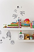 Detail of children's books and toys on white floating shelves with various decorative stickers on wall