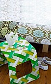 Curved plastic stool covered with green and white patterned fabric next to bed with floral-upholstered frame