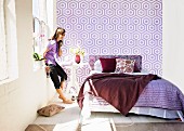 Sonniges Schlafzimmer mit verschiedenen Violetttönen auf Bettwäsche und grafisch gemusterter Wandtapete