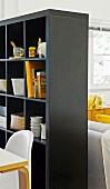 Black shelving with storage for crockery and books as partition between dining and lounge areas