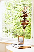 Aufgefädelte Holz Fundstücke vor Fenster aufgehängt, im Vordergrund Beistelltisch mit Buch und gerahmtes Photo