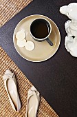 Kaffeetasse mit Unterteller auf schwarzem Tablett, daneben Damenschuhe auf Sisalteppich