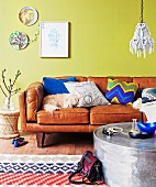 Dog sleeping on retro leather sofa with various scatter cushions against lime green wall, decorative wall plates, wooden floor and rug with geometric pattern