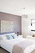 Double bed with bedspread below modern artwork on wall painted pale grey in simple bedroom