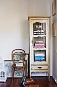 Handbag on floor in front of Thonet chair and antique display cabinet of books in corner of room