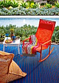 Orange rocking chair on blue carpet next to side table with cocktail glasses in front of pool