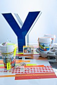Large, blue, ornamental letter on colourful place mat and paper cups with comic-page print