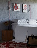 Double bed below red and white floral paintings and innovative sconce lamps on brick wall painted dark grey