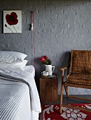 Innovative sconce lamp on grey-painted brick wall above bed with wooden crate used as bedside table and armchair