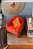 Looking down from a stairway at an orange, velvet armchair with plush cushions and decorative 'sun' with stylized rays