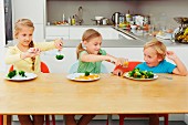 Drei Kinder spielen mit Gemüse am Tisch in der Küche
