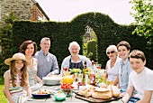 Multigenerational family sitting around table decked with food in a summer garden