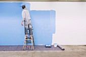 Man standing on ladder painting wall blue