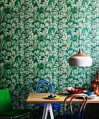 Retro lamp above dining table with Thonet chairs partially dipped in paint against leaf-patterned wallpaper