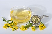 Goldenrod tea in a glass cup, dried tea leaves and fresh flowers