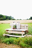 Two milk churns on wooden bench on edge of meadow