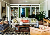 Country-house living room with various upholstered chairs and comfortable sofa in mixture of patterns around oval wooden coffee table and black and white geometric rug