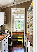 Country-house-style galley kitchen with view of writing desk and yellow stool through doorway