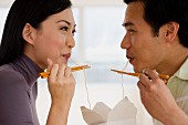 Asian couple eating noodles with chopsticks