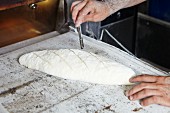 A baker scoring unbaked bread with a razor blade