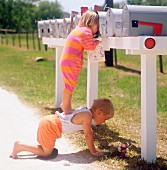 Little girl standing on brother's back peering into post box