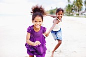 Two dark-skinned girls running along beach hand in hand