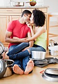 Couple kissing on kitchen floor surrounded by pots and pans